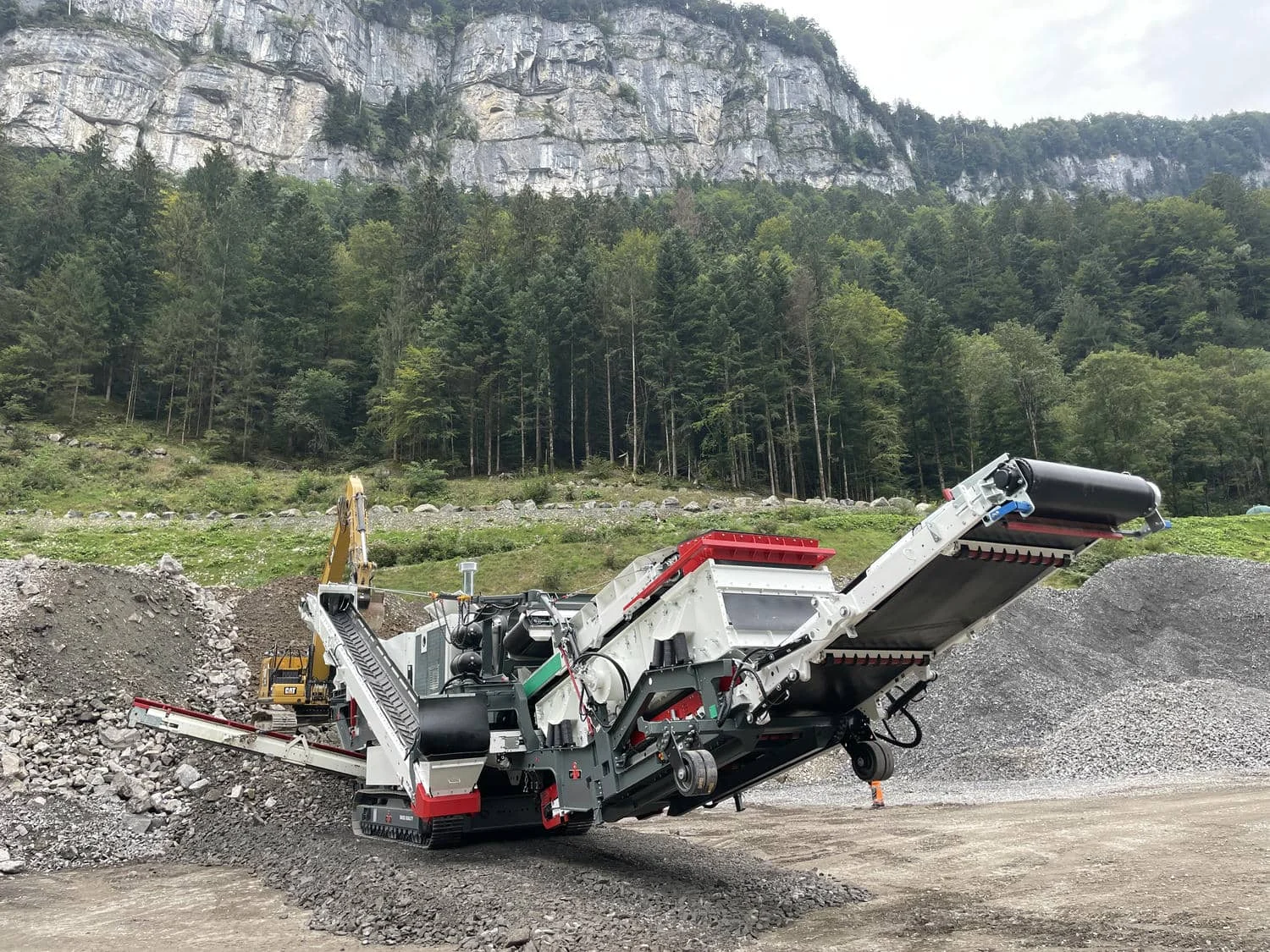 Mobile Brechanlage in alpinem Gelände, Bagger beschickt den Backenbrecher mit Gestein.