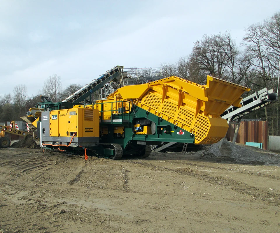 Gipo B0960 Giga Concasseur à mâchoires mobile en carrière, alimenté par pelle ; convoyeurs stockant la roche concassée.