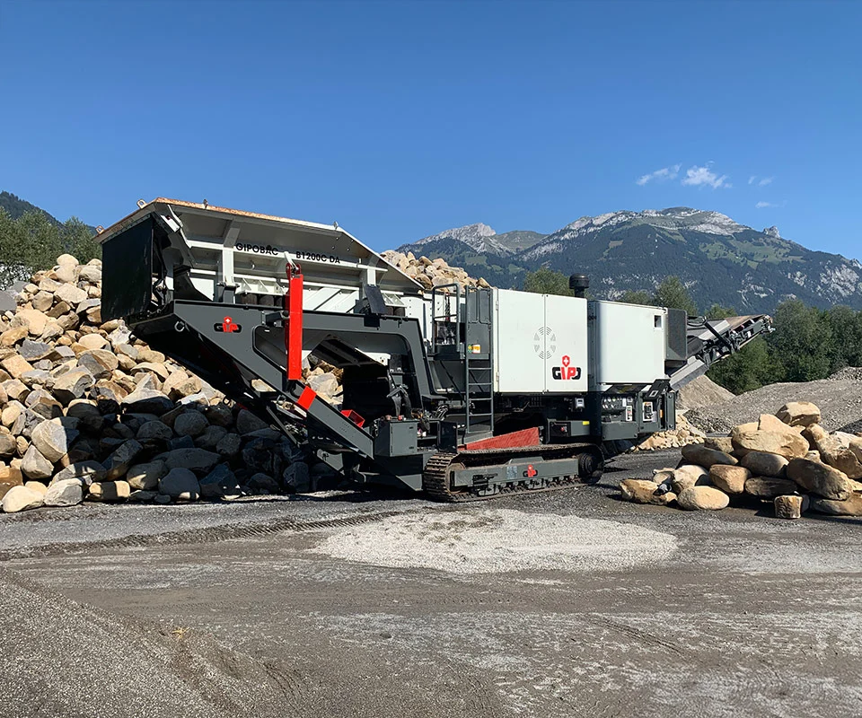 Gipo B1270 Mobile jaw crushing plant on tracks, processing blasted rock; discharge conveyors forming piles.