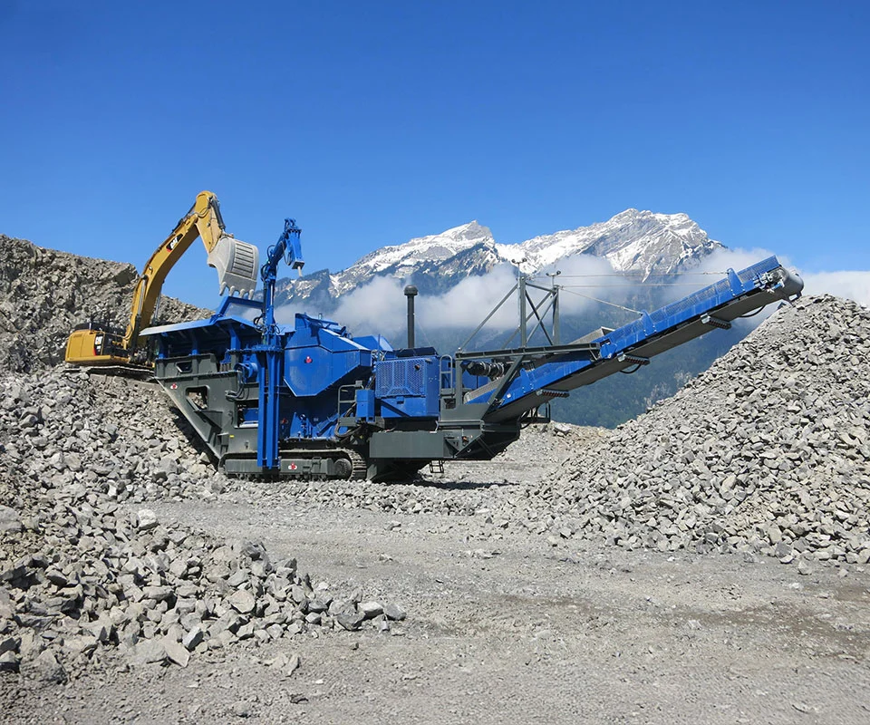 Gipo B14100 Mobile jaw crushing plant on tracks, processing blasted rock; discharge conveyors forming piles.