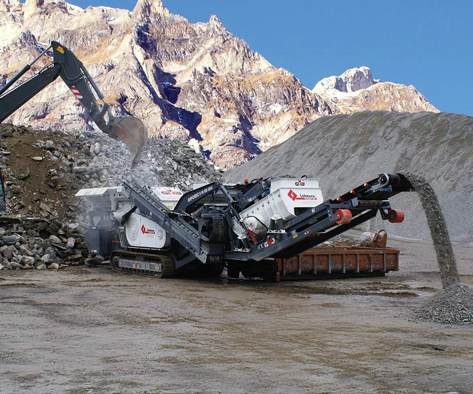 Gipo P090 Giga Concasseur à percussion mobile GIPO en carrière, alimenté par pelle; convoyeurs formant des tas de granulats.