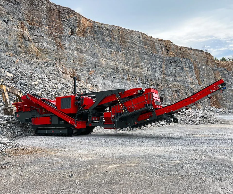 Gipo P130 Giga Concasseur à percussion mobile GIPO en carrière, alimenté par pelle; convoyeurs formant des tas de granulats.