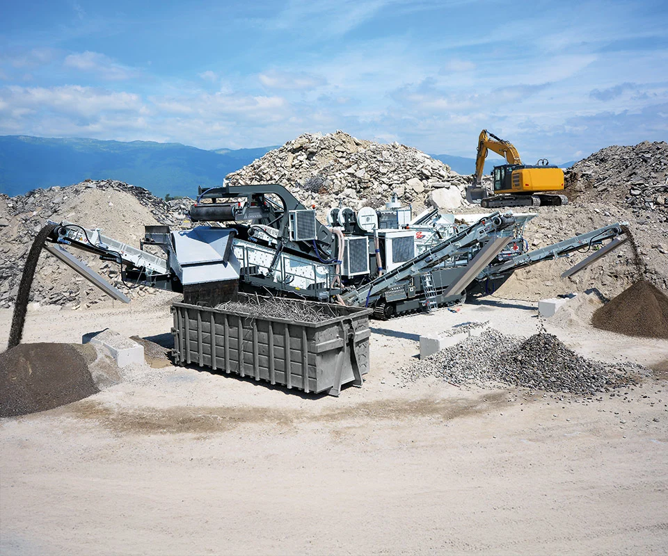 Gipo P130 Giga Concasseur à percussion mobile GIPO en carrière, alimenté par pelle; convoyeurs formant des tas de granulats.