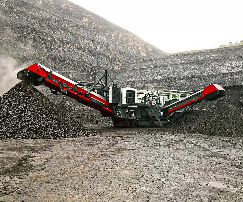 Gipo P150 Concasseur à percussion mobile GIPO en carrière, alimenté par pelle; convoyeurs formant des tas de granulats.