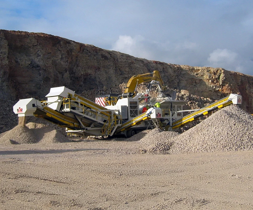 Gipo P170Concasseur à percussion mobile GIPO en carrière, alimenté par pelle; convoyeurs formant des tas de granulats.